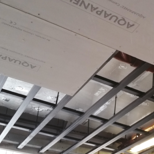 Suspended metal ceiling grid being fitted with acoustic ceiling insulation tiles.