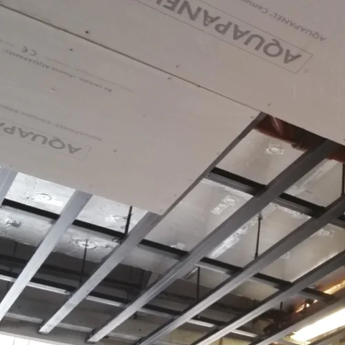 Suspended metal ceiling grid being fitted with acoustic ceiling insulation tiles.