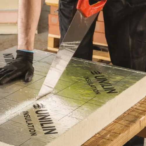 Person cutting a foil-faced PIR insulation board with a handsaw.