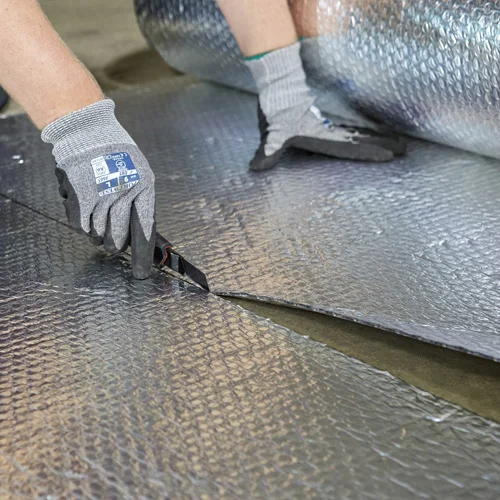 Gloved hands unrolling a roll of reflective multifoil insulation.