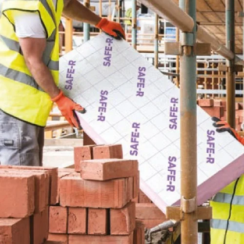 Construction worker carrying a pink phenolic insulation board on site.