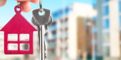 Hand holding a set of house keys with a building in the background