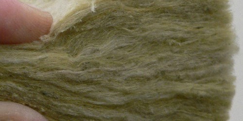 Hand holding a sample of yellow glass wool insulation
