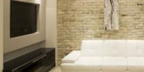 Modern furnished basement living room with white sofas and stone walls