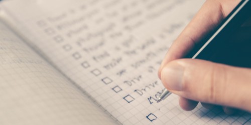 Person writing on a checklist in a notebook
