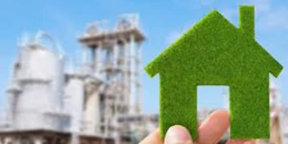 Hand holding a green house cutout against a blurred industrial background