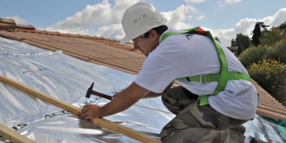 Roofer installing shiny multifoil insulation on a roof