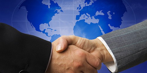 Two business people shaking hands against a blue world map background