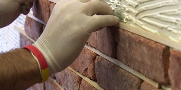 Gloved hands pointing or working on a brick wall