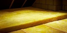 Yellow loft insulation rolls installed between floor joists in an attic space