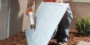 Worker installing blue rigid insulation boards on a foundation wall