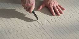 Hands scoring a cement backer board with a utility knife