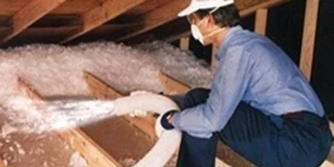 Worker spraying loose-fill insulation into an attic space