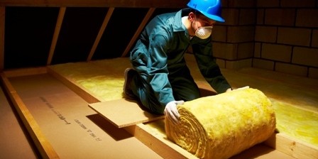 Worker installing yellow insulation rolls in a confined loft space