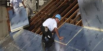 Worker installing silver insulation boards on a metal roof deck