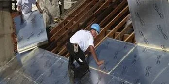 Worker installing silver insulation boards on a metal roof deck
